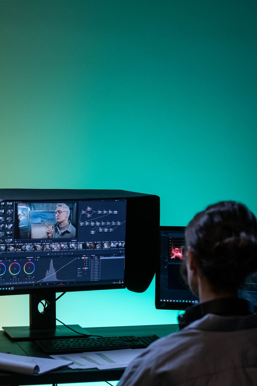 A team of directors, sound mixers, and script supervisors monitoring video playback screens in an dark interior editing room environment